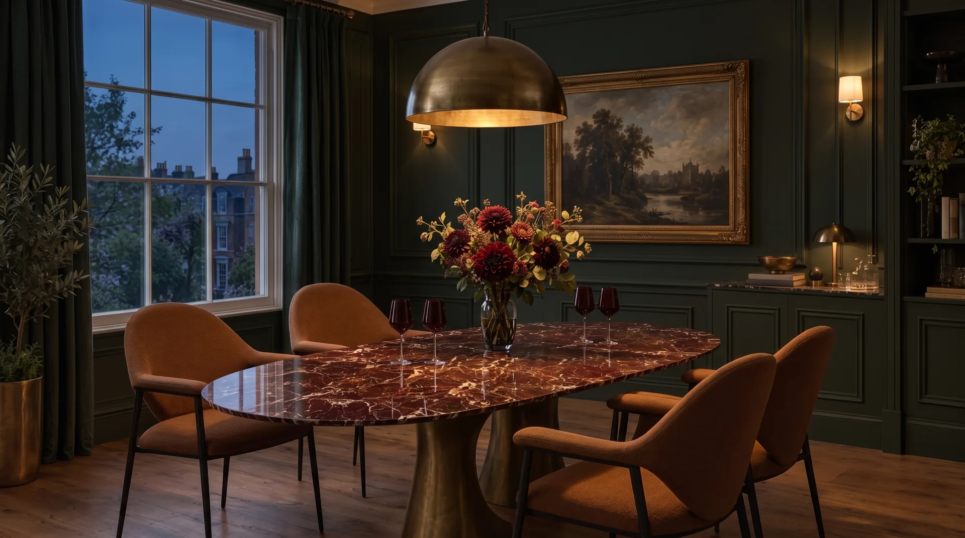 Forest green dining room at dusk lit by a low aged brass dome pendant over an oval Venus Vein porcelain table, its glossy burgundy top reflecting the light, with dark dahlias, red wine glasses and cognac upholstered chairs