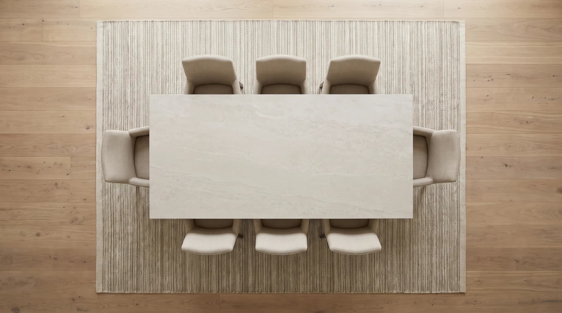 Overhead view of a rectangular stone-effect dining table and six tucked-in chairs centred on a large flat-weave rug over an oak floor, with an even margin of rug on every side
